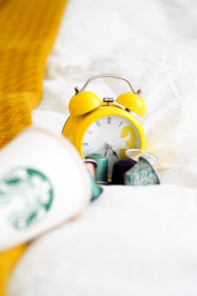 Yellow alarm clock beside a white ceramic cup
